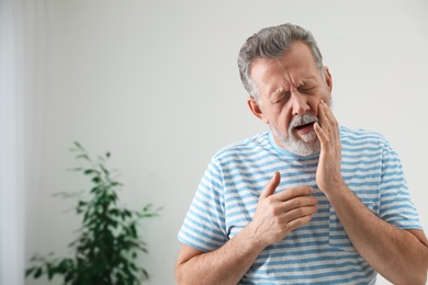 Mature man suffering from strong tooth pain at home, space for text