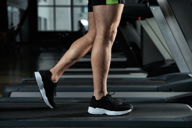 Photo of Man working out on treadmill in modern gym, closeup of legs