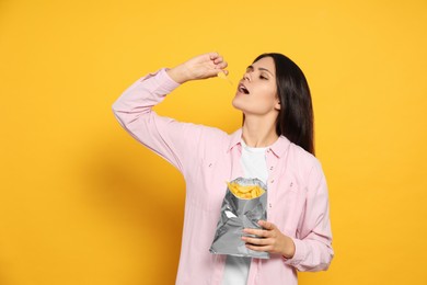 Beautiful woman eating potato chips on orange background