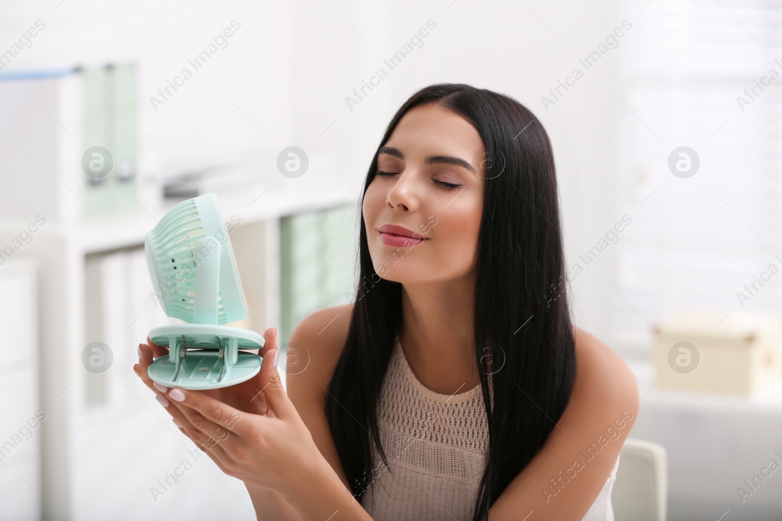 Photo of Young woman enjoying air flow from fan at workplace