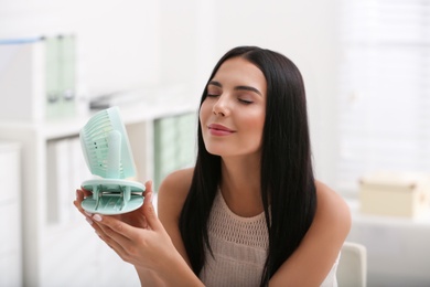 Young woman enjoying air flow from fan at workplace