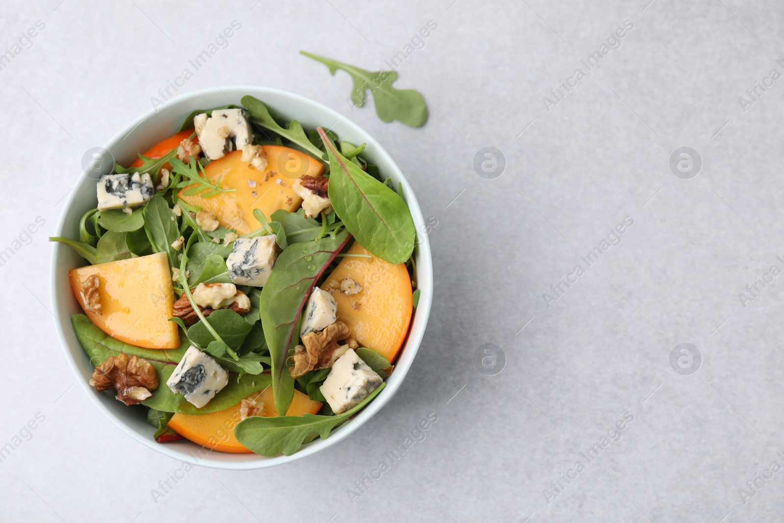 Photo of Tasty salad with persimmon, blue cheese and walnuts served on white table, top view. Space for text