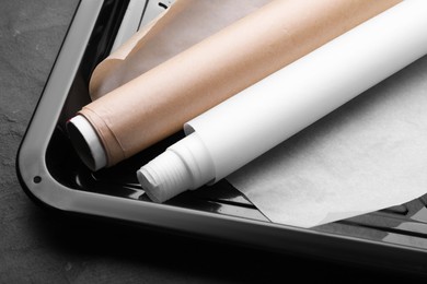 Baking pan with rolls of parchment paper on black table, closeup