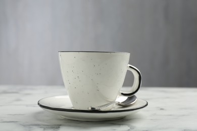 Photo of Coffee cup, spoon and saucer on white marble table, closeup