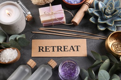 Photo of Card with word Retreat, burning candle and different spa products on dark grey table, above view