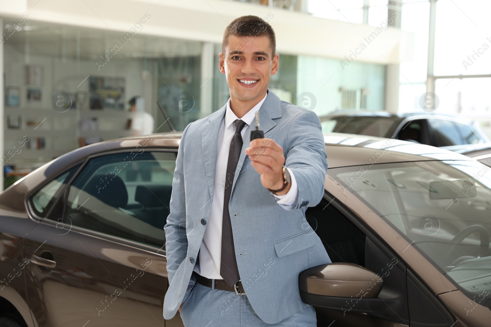 Photo of Young salesman with key near car in modern dealership