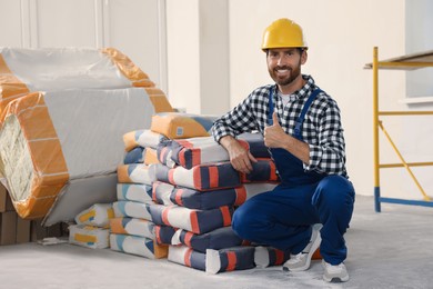 Photo of Professional builder in uniform near cement bags indoors