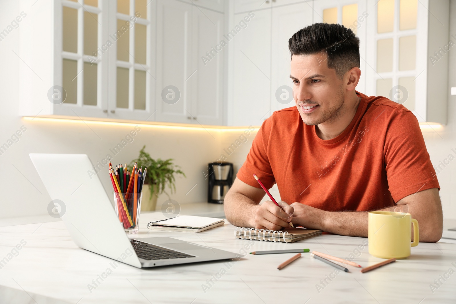 Photo of Man drawing in notebook at online lesson indoors. Distance learning