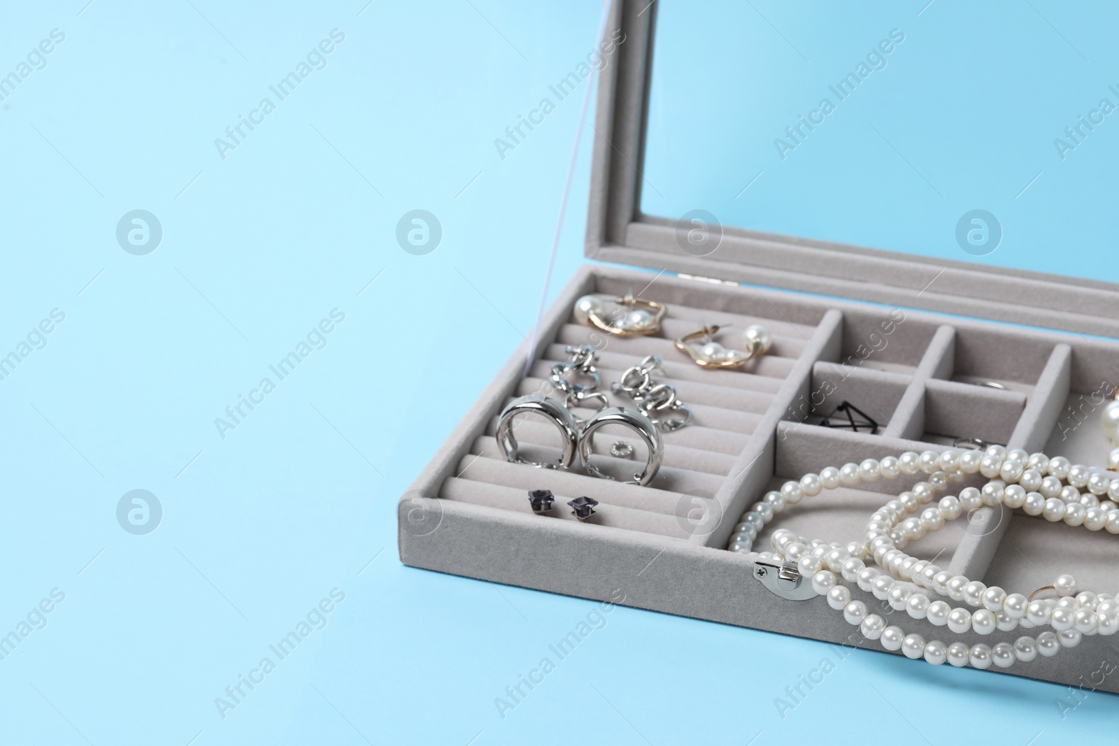 Photo of Jewelry box with many different accessories on light blue background, space for text