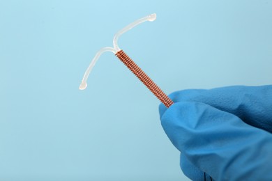 Photo of Doctor holding T-shaped intrauterine birth control device on light blue background, closeup