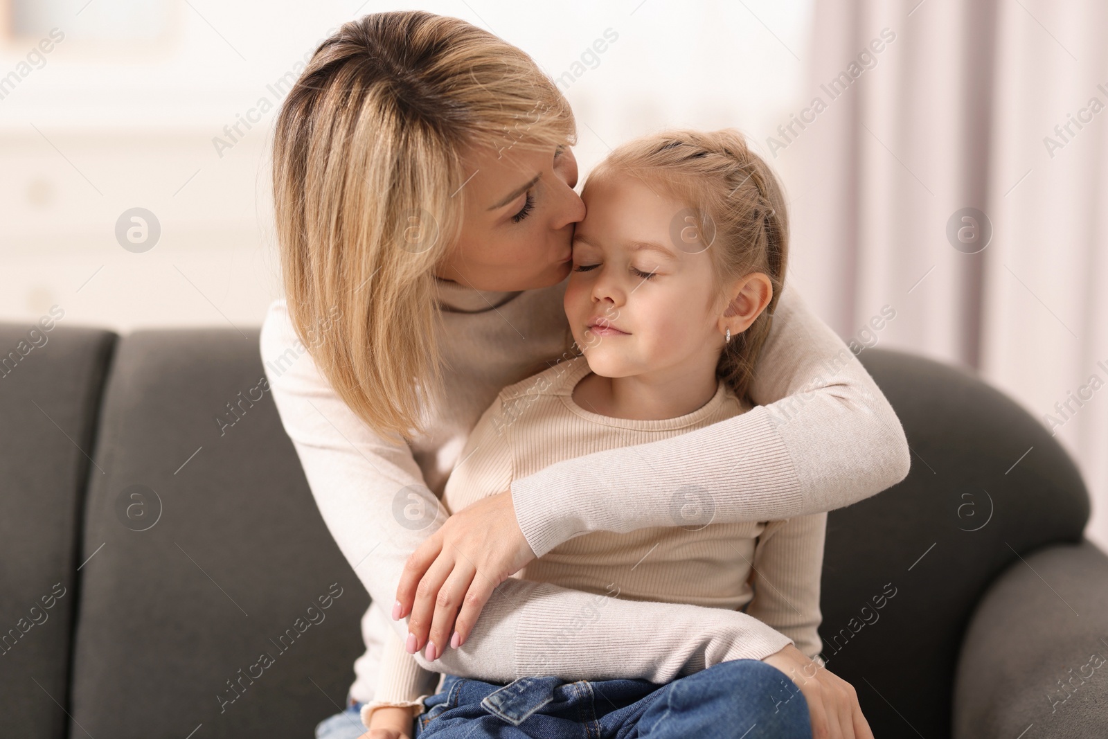 Photo of Mother kissing her daughter on sofa at home