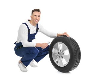 Male mechanic with car tire on white background