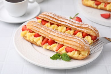 Photo of Delicious eclairs filled with cream, strawberries and mint on white tiled table