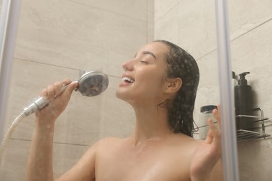 Photo of Washing hair. Happy woman with showerhead singing indoors, view through wet glass