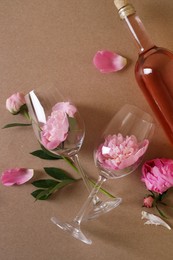Bottle of rose wine, glasses and beautiful pink peonies on brown background, flat lay
