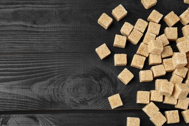 Photo of Brown sugar cubes on black wooden table, flat lay. Space for text