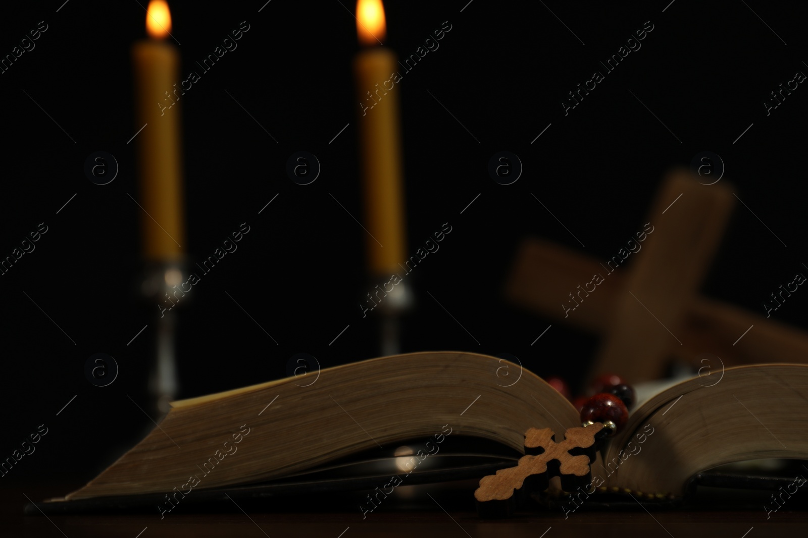 Photo of Wooden cross, rosary beads, Bible and church candles on table, closeup