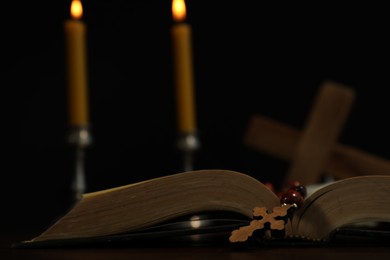 Wooden cross, rosary beads, Bible and church candles on table, closeup