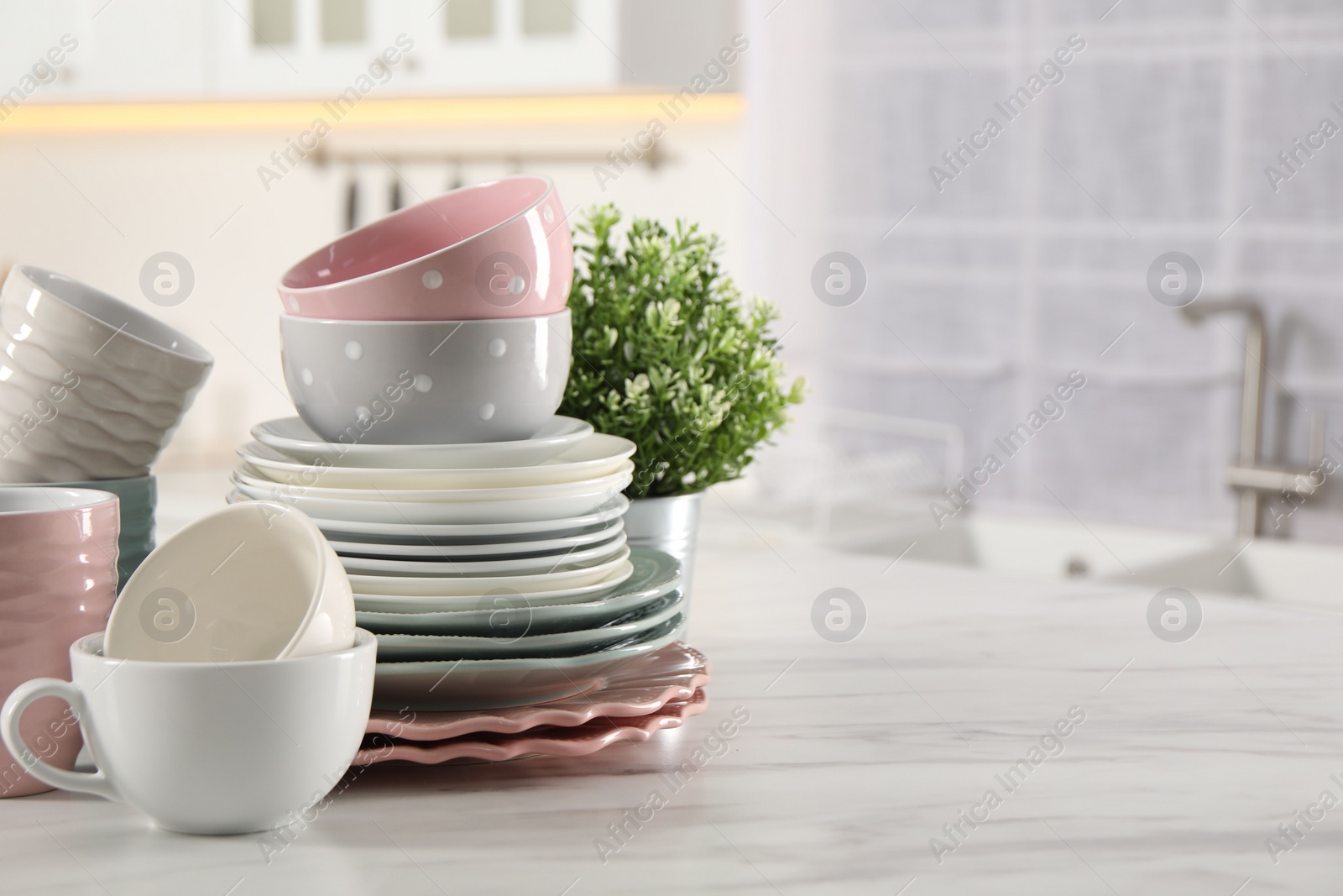 Photo of Many different clean dishware, cups and houseplant on white marble table in kitchen. Space for text