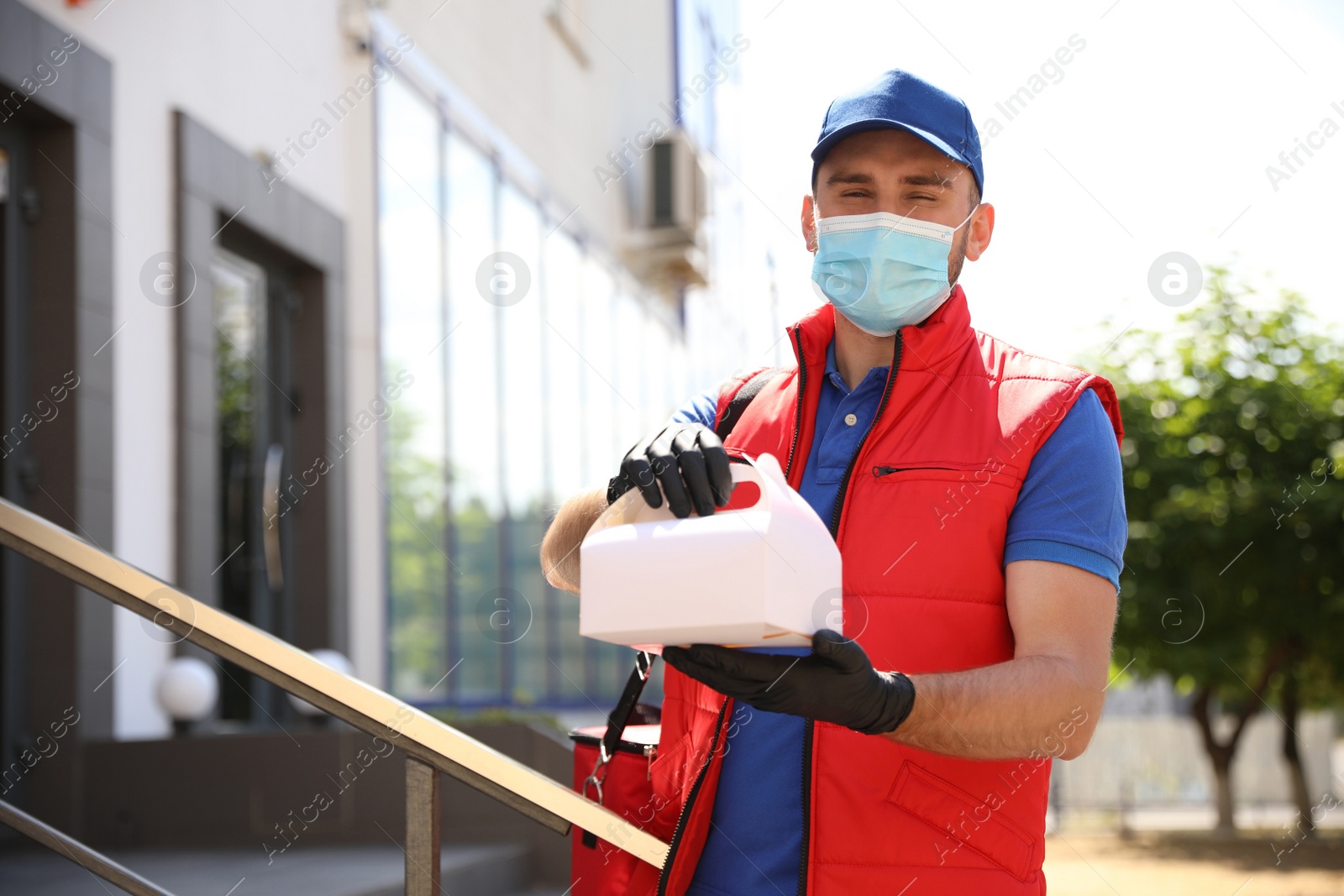 Photo of Courier in protective mask and gloves with order outdoors. Restaurant delivery service during coronavirus quarantine