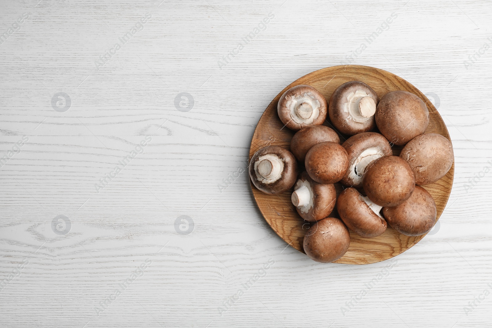 Photo of Plate with fresh champignon mushrooms on wooden table, top view. Space for text