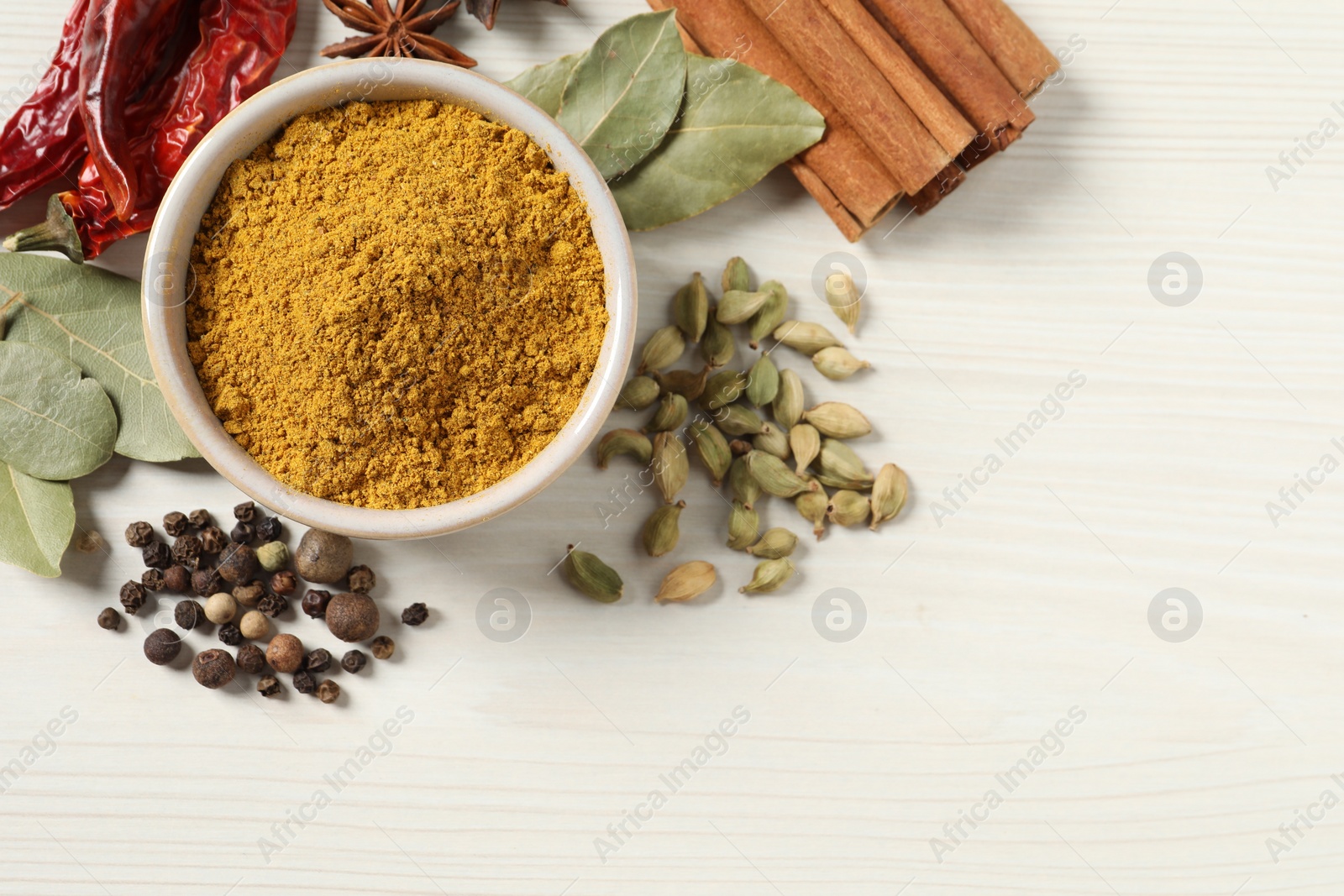 Photo of Curry powder in bowl and other spices on white wooden table, flat lay. Space for text