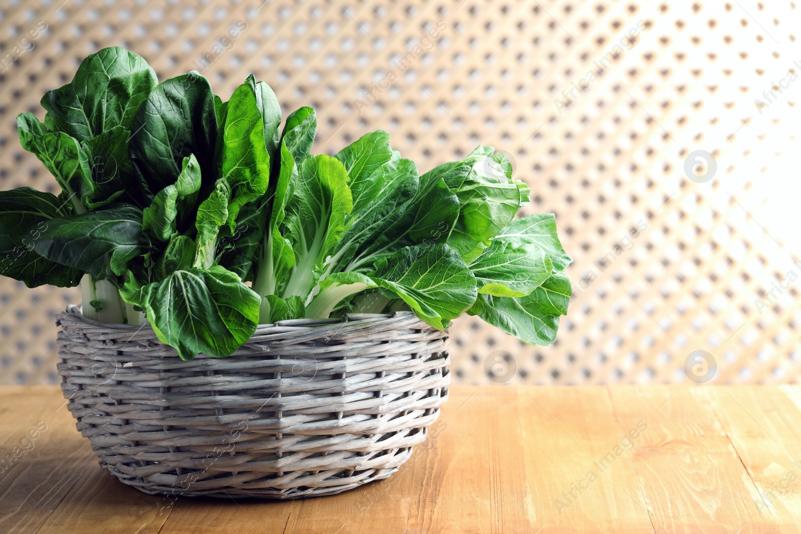 Photo of Fresh green pak choy cabbages in wicker basket on wooden table, space for text