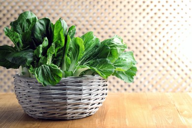 Photo of Fresh green pak choy cabbages in wicker basket on wooden table, space for text