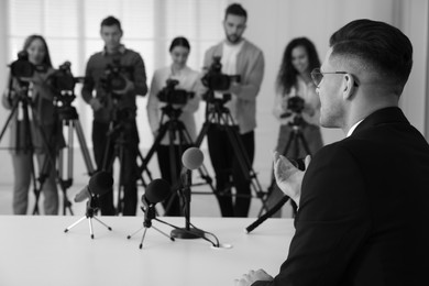 Image of Businessman giving interview to journalists indoors. Black and white effect