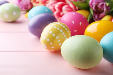 Photo of Bright painted eggs and spring tulips on pink wooden table, closeup. Happy Easter
