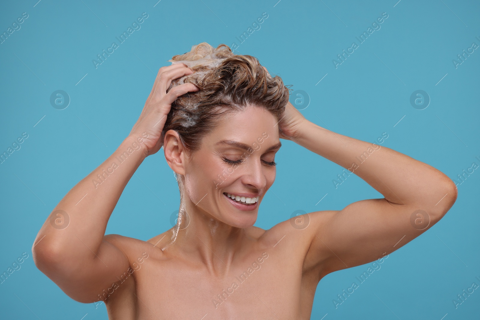 Photo of Beautiful happy woman washing hair on light blue background