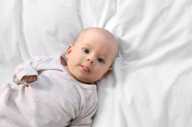 Photo of Cute little baby lying on white sheets, top view. Space for text