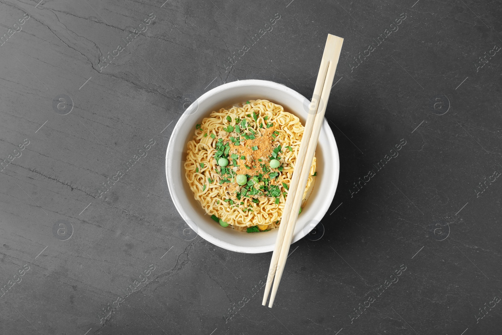Photo of Cup of instant noodles with chopsticks on grey background, top view