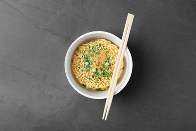 Photo of Cup of instant noodles with chopsticks on grey background, top view