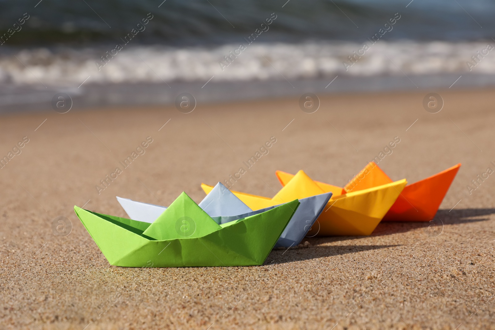 Photo of Bright colorful paper boats on sandy beach near sea