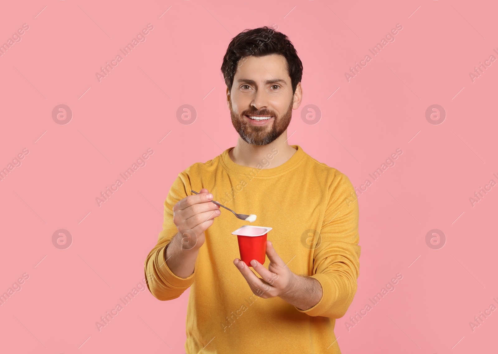 Photo of Handsome man with delicious yogurt and spoon on pink background