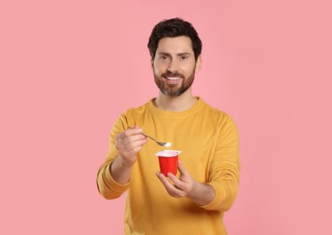 Handsome man with delicious yogurt and spoon on pink background