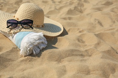 Photo of Straw hat, towel and sunglasses on sand. Space for text