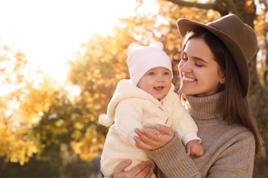 Happy mother with her baby daughter in park on sunny autumn day, space for text