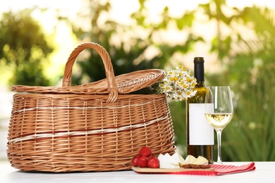 Picnic basket and wine with products on table against blurred background