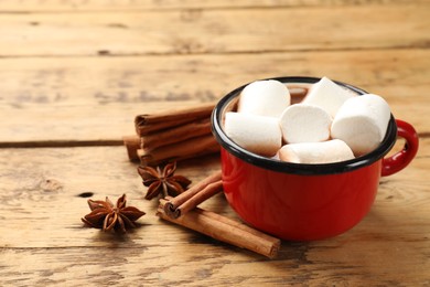 Photo of Tasty hot chocolate with marshmallows and spices on wooden table, closeup. Space for text