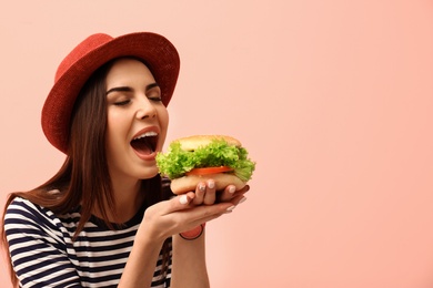 Young woman eating tasty burger on color background. Space for text