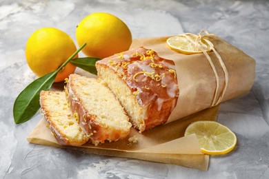 Photo of Cut tasty lemon cake with glaze and citrus fruits on light grey textured table