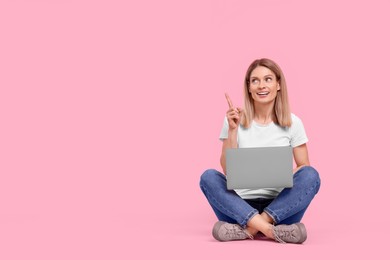 Photo of Happy woman with laptop pointing at something on pink background. Space for text