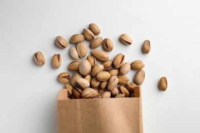 Photo of Overturned paper bag with pistachio nuts on white background, flat lay