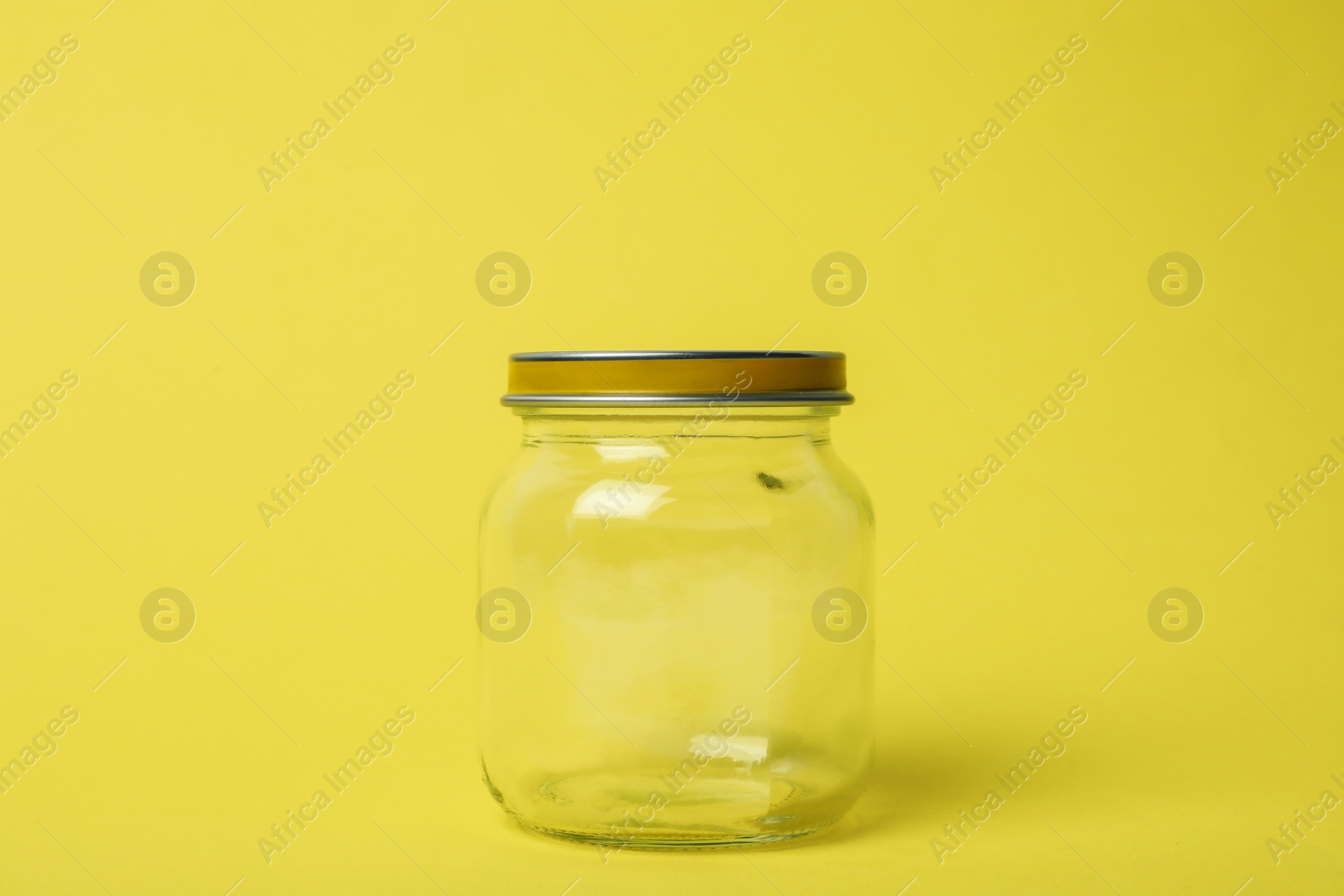 Photo of Closed empty glass jar on light yellow background