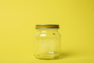 Closed empty glass jar on light yellow background