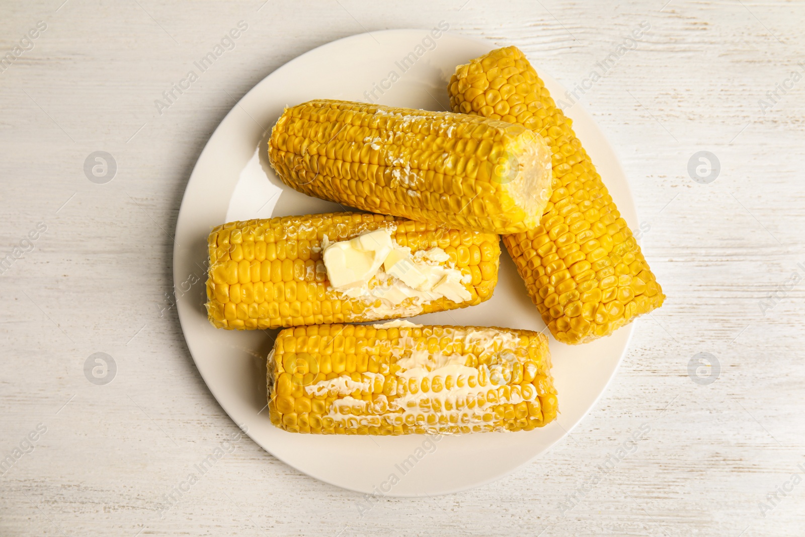 Photo of Delicious boiled corn with butter on white wooden table, top view