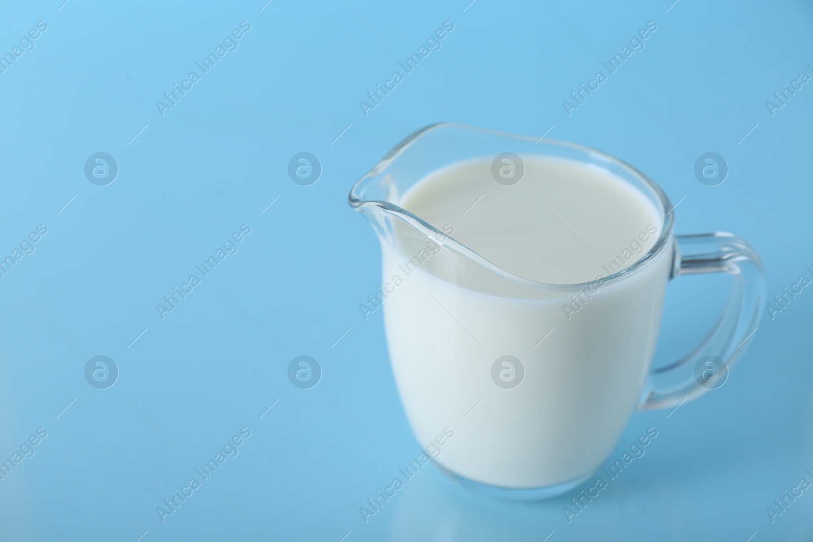 Photo of Jug of fresh milk on light blue background, closeup. Space for text