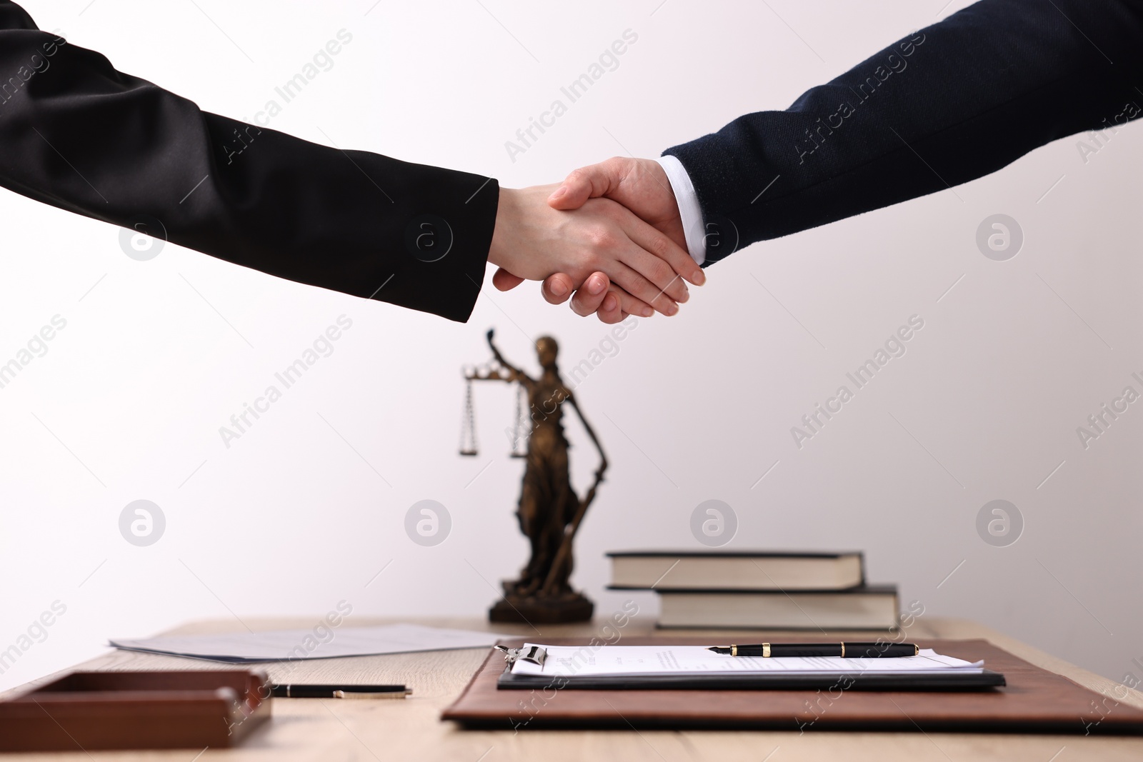 Photo of Notary shaking hands with client at wooden table in office, closeup